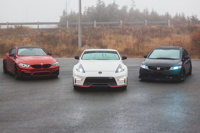 BMW, Nissan, and Honda parked beside each other with bright headlights on